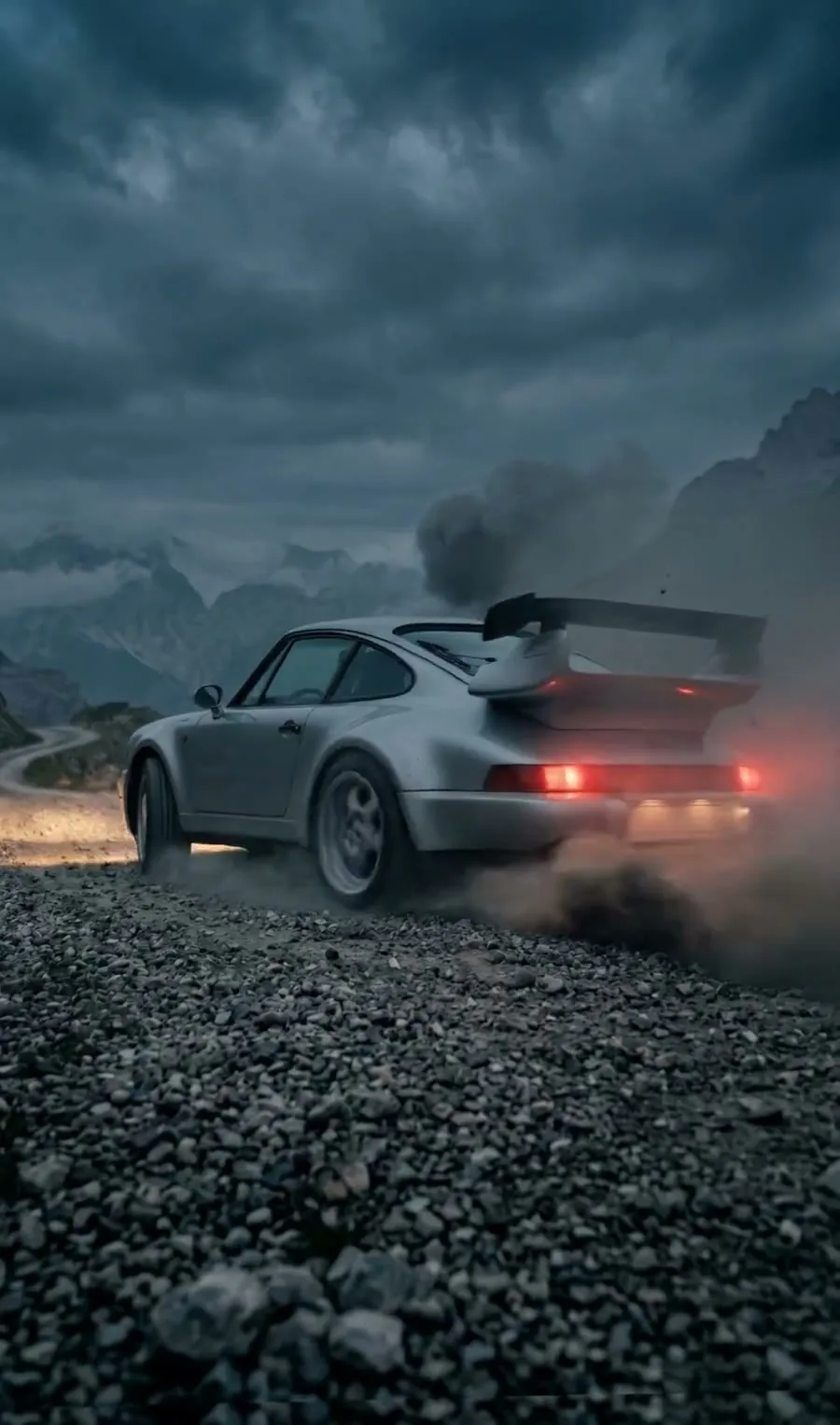A silver sports car with a rear wing sliding across a gravel road, dust rising behind it, mountains in the distance