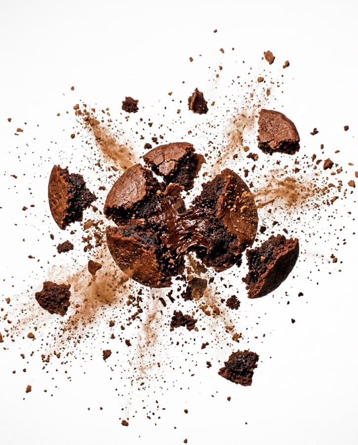 A brownie breaking apart mid-air with cocoa scattering